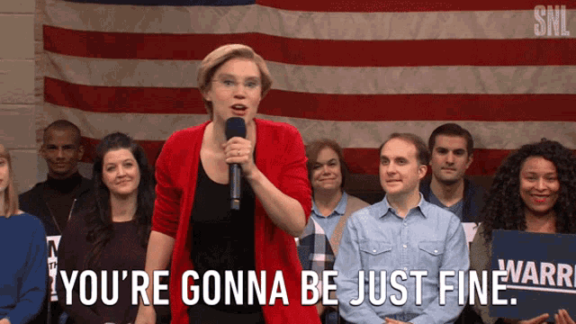 a woman stands in front of a crowd holding a microphone and saying you 're gonna be just fine