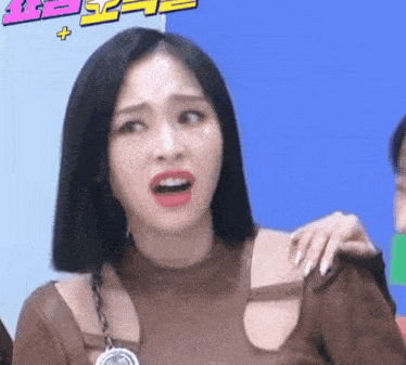a woman with short black hair is making a funny face with her mouth open and her hand on her shoulder .