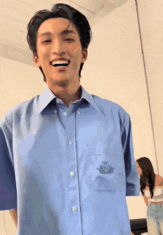 a young man wearing a blue shirt with a logo on the sleeve is smiling