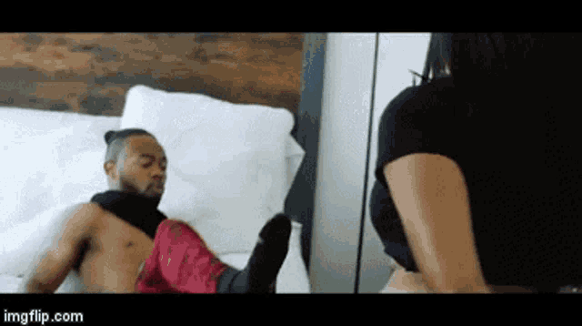 a woman is standing next to a shirtless man on a bed