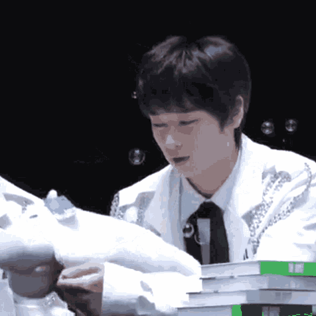 a man in a white suit and tie is sitting in front of a stack of books