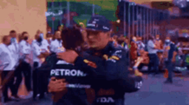 a man in a petron shirt is hugging another man in a crowd