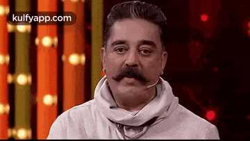 a man with a mustache and a microphone around his neck is looking at the camera .