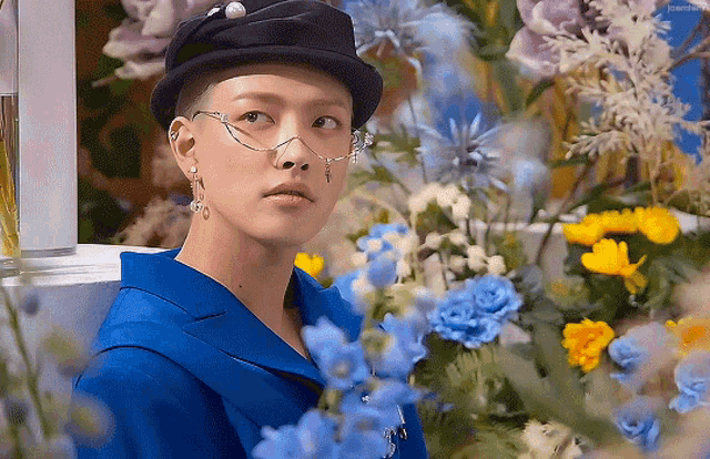 a man wearing a hat and glasses is surrounded by blue flowers .