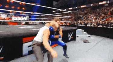 two men are wrestling in a wrestling ring with a crowd in the background .