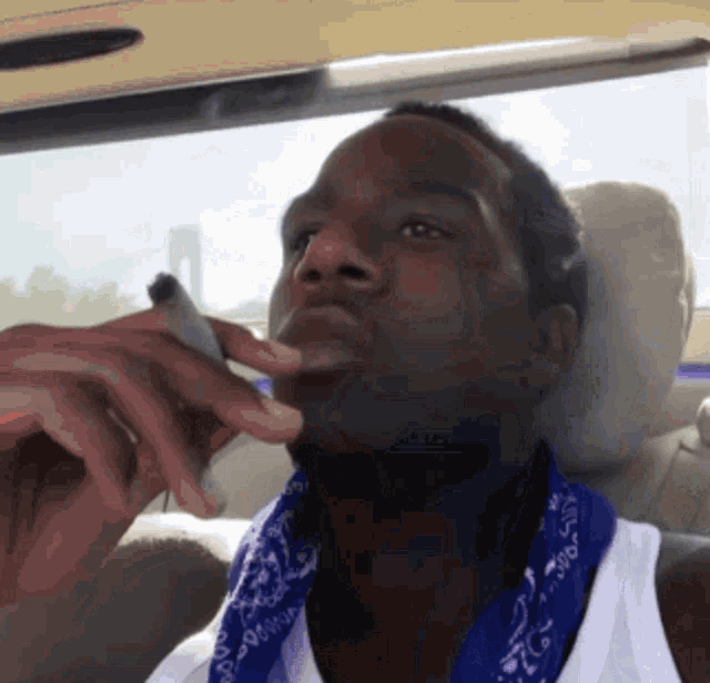 a man wearing a bandana and a white tank top is smoking a cigarette