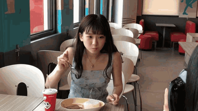 a girl is sitting at a table with a jollibee cup in front of her