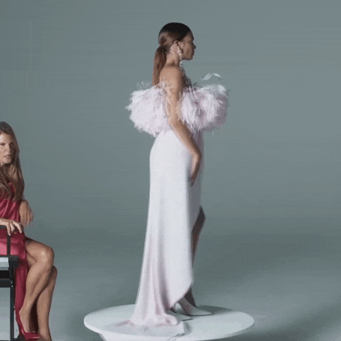 a woman in a white dress with feathers on the shoulders is standing next to another woman in a red dress