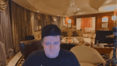 a man in a black shirt is sitting in a living room looking at the camera