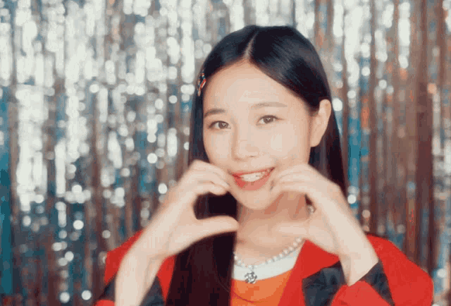 a woman making a heart with her hands in front of a sequined backdrop