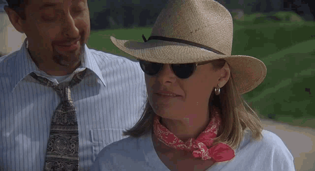 a woman wearing a hat and sunglasses stands next to a man
