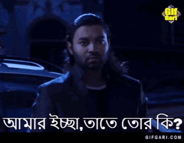 a man with long hair and a beard is standing in front of a car and says " gifgari.com " on the bottom