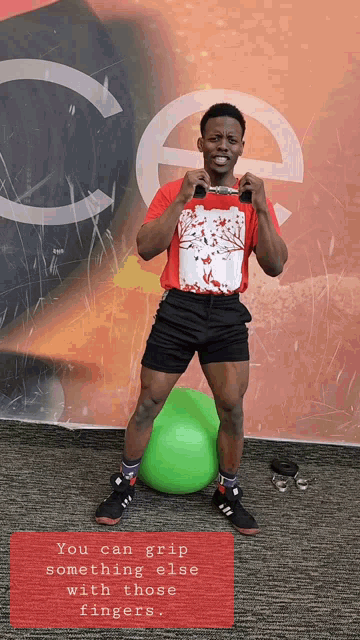 a man in a red shirt and black shorts stands next to a green exercise ball