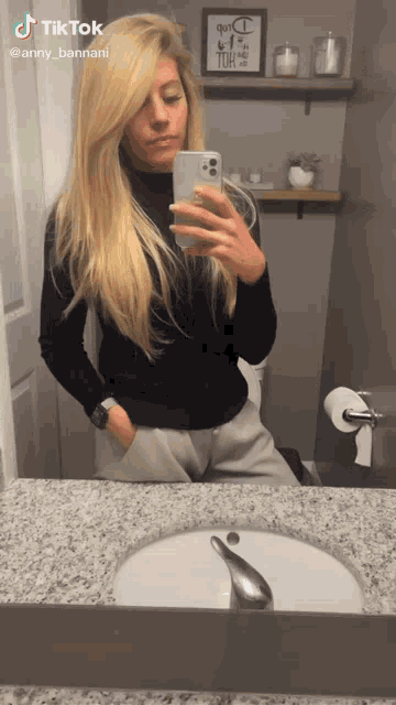 a woman taking a selfie in front of a bathroom mirror with a tiktok logo