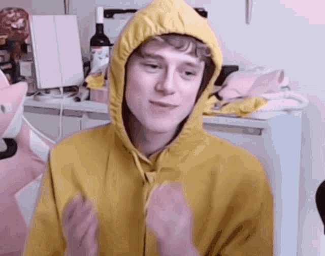 a young man wearing a yellow hoodie is sitting in front of a mirror and a bottle of wine .