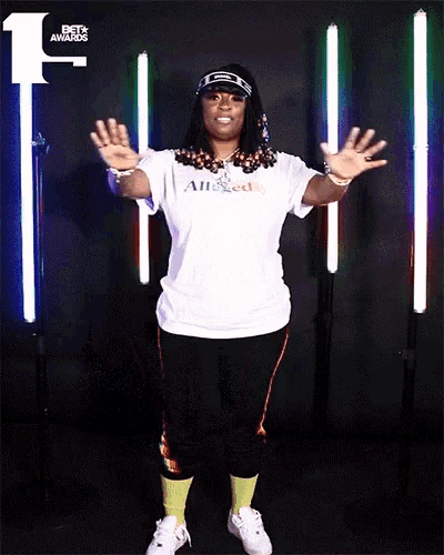 a woman wearing a white alleged t-shirt stands in front of a row of lights