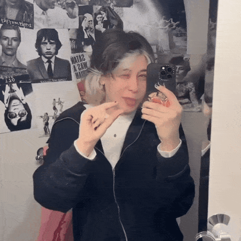 a woman taking a picture of herself in front of a wall with posters of famous people including one that says mata2