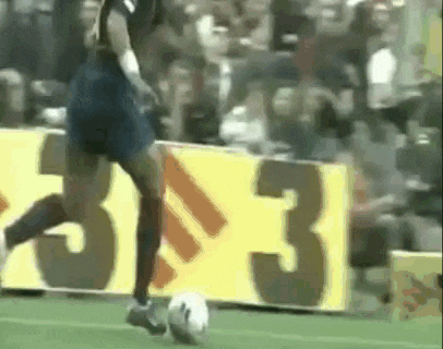 a soccer player is kicking a soccer ball on a field in front of a yellow sign with the number 33 on it .