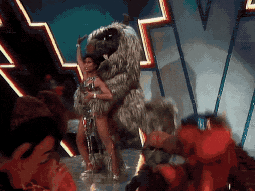 a woman is riding a stuffed animal on a stage in front of a crowd