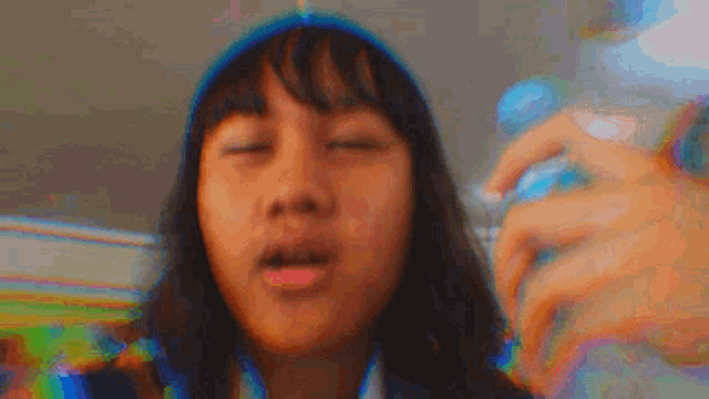 a young girl is taking a selfie with her eyes closed and holding a bottle of water .