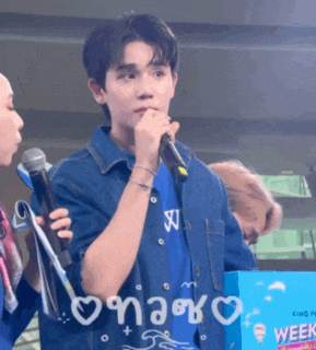 a man in a blue shirt is holding a microphone in front of a box that says week