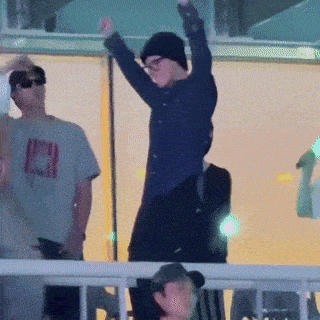 a man in a black hat is dancing in front of a crowd with his arms in the air