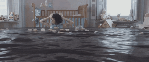 a woman is sitting in a flooded room with a crib