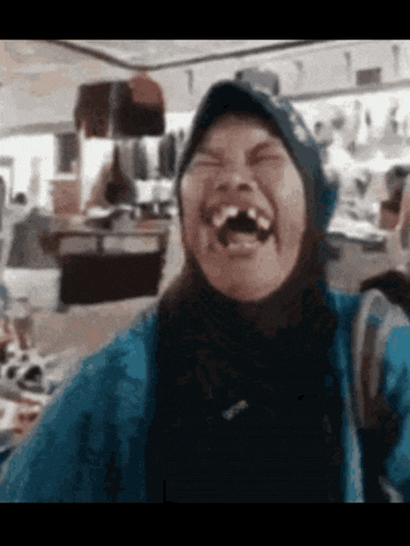 a woman wearing a blue jacket and a hat is laughing with her mouth open