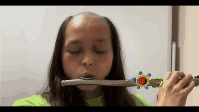 a girl with a bald head plays a flute in front of a white board