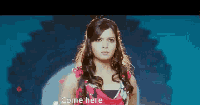a woman in a red dress is standing in front of a blue background with the words `` come here '' written on it .