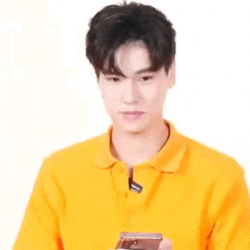 a young man in a yellow shirt is holding a cell phone .
