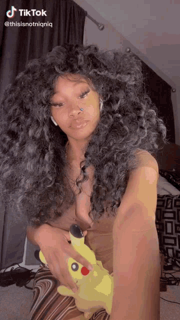 a woman with curly hair is holding a yellow pikachu stuffed animal .