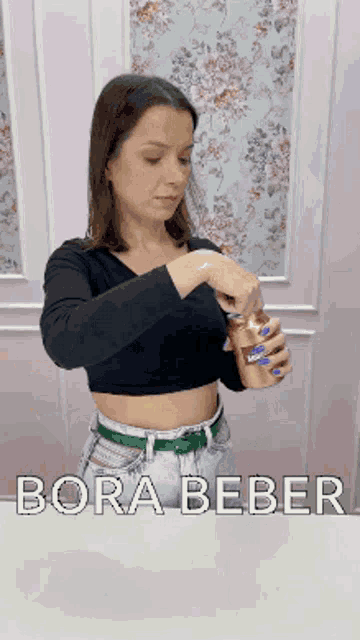 a woman in a black crop top is opening a can of bora beber .