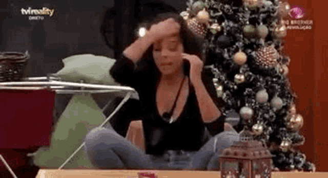 a woman is sitting on a table with her legs crossed in front of a christmas tree .