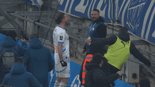 a man wearing a yellow vest that says puma on it talks to another man