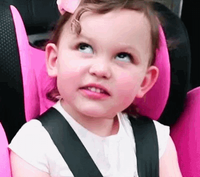 a little girl is sitting in a pink car seat looking up at the sky .