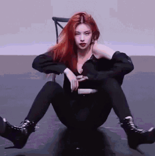 a woman with red hair is sitting on the floor wearing black leggings and boots .