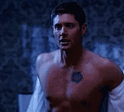 a shirtless man with a tattoo on his chest is standing in front of a patterned wall .