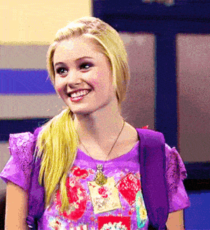 a blonde girl wearing a purple shirt and a backpack smiles