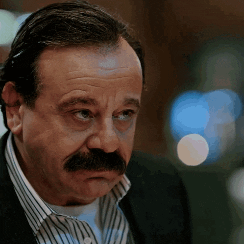 a man with a mustache is wearing a suit