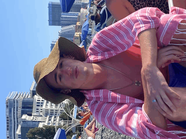 a man wearing a hat and a pink and white striped shirt is sitting on a beach