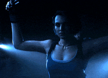 a woman in a blue tank top holds a gun in a dark room