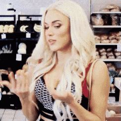 a woman with blonde hair is standing in front of a grocery store holding something in her hands .