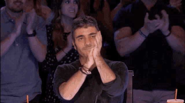 a man is clapping his hands while sitting in a crowd .
