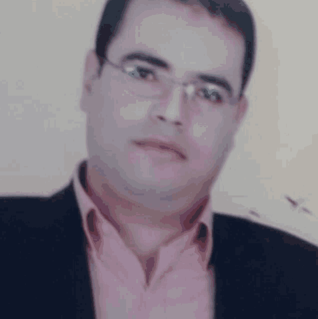 a man with glasses and a pink shirt is wearing a black jacket