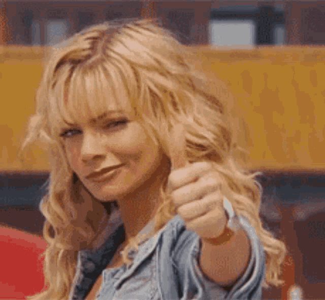 a woman is giving a thumbs up sign while wearing a denim jacket .