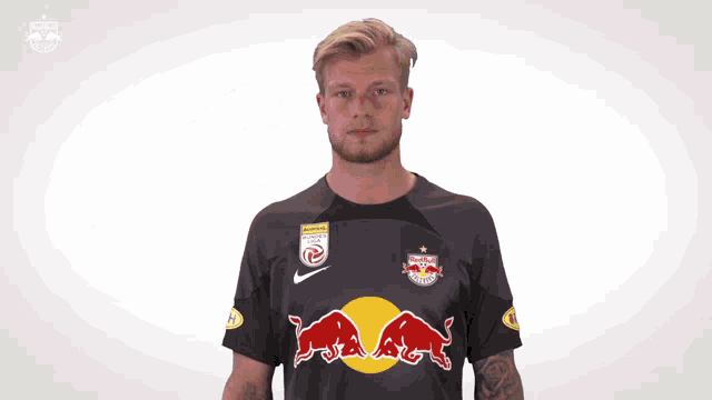 a man wearing a red bull jersey holds a tennis ball in his hand
