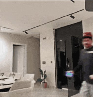 a man in a red hat is standing in a living room holding a phone .