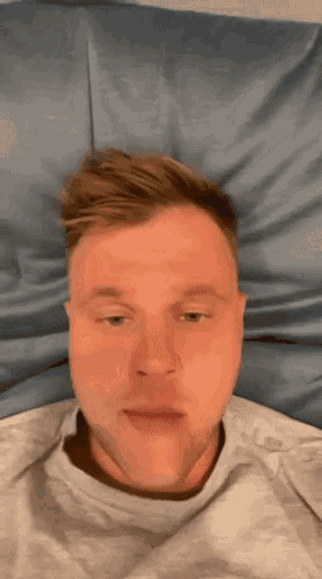 a man laying on a bed with his eyes closed and a gray shirt on