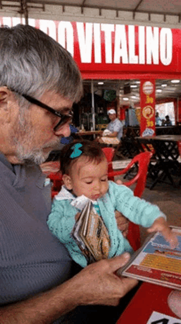 a man is holding a baby in front of a restaurant that says vitalino
